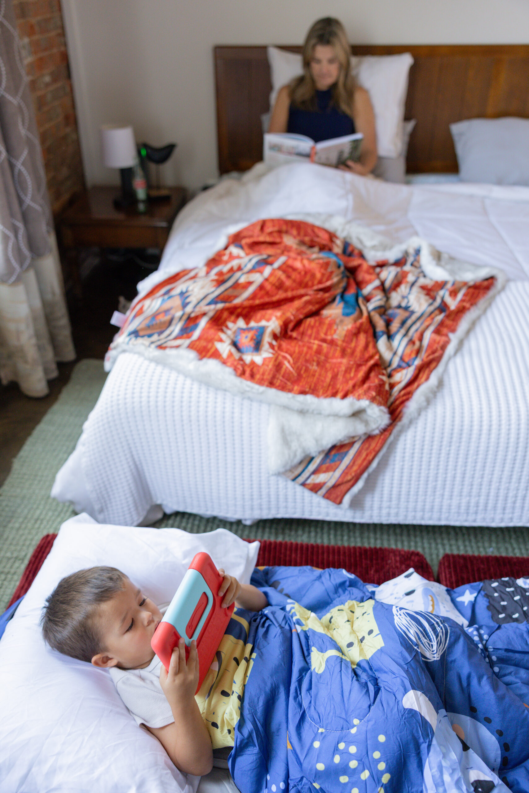 Young kid laying on dark red ottoman configured into a bed watching his ipad.