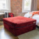 Dark red ottoman sitting in a room with a brick wall.