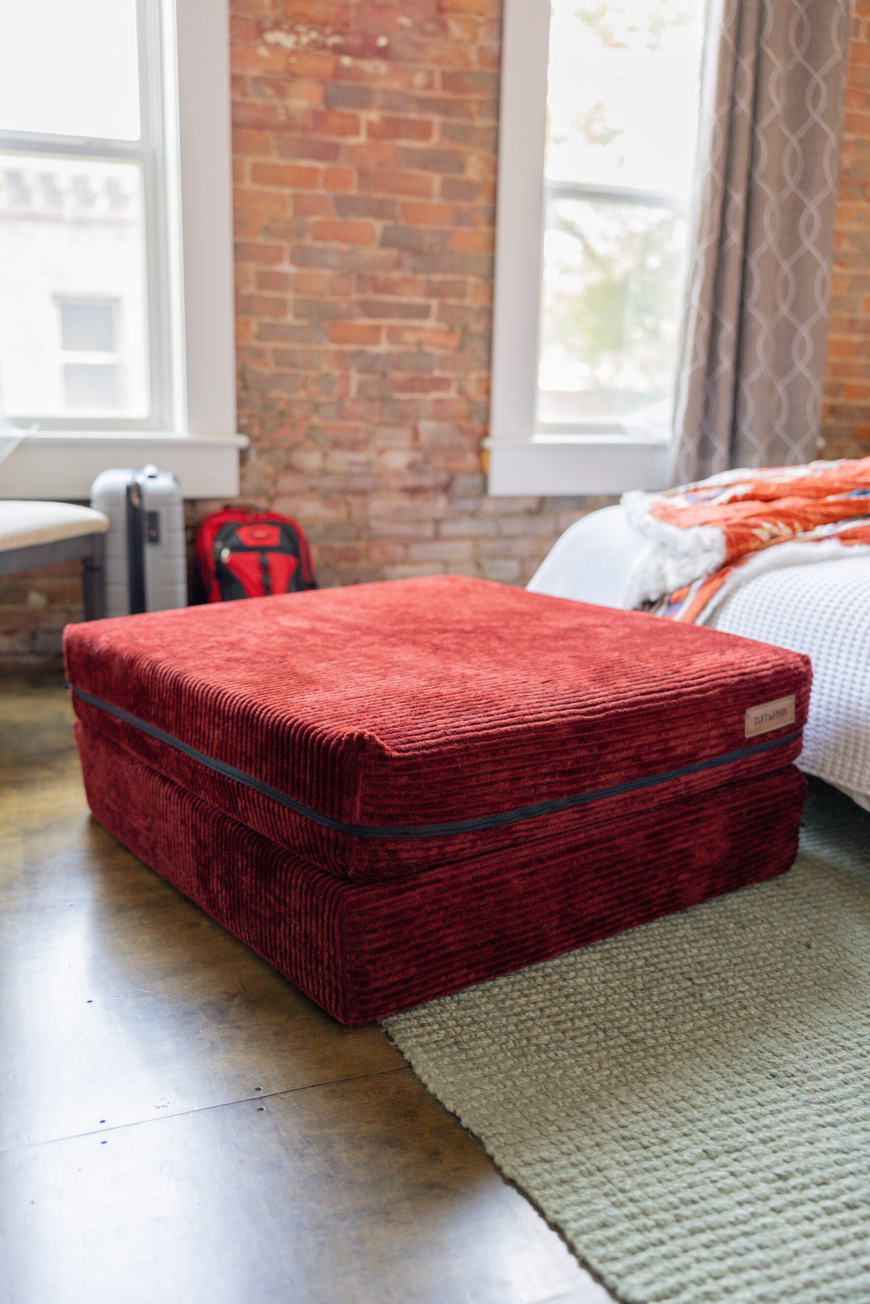 Dark red ottoman sitting in a room with a brick wall.