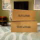 Two large boxes stacked ontop of each other in a living room that say tuft & Finch