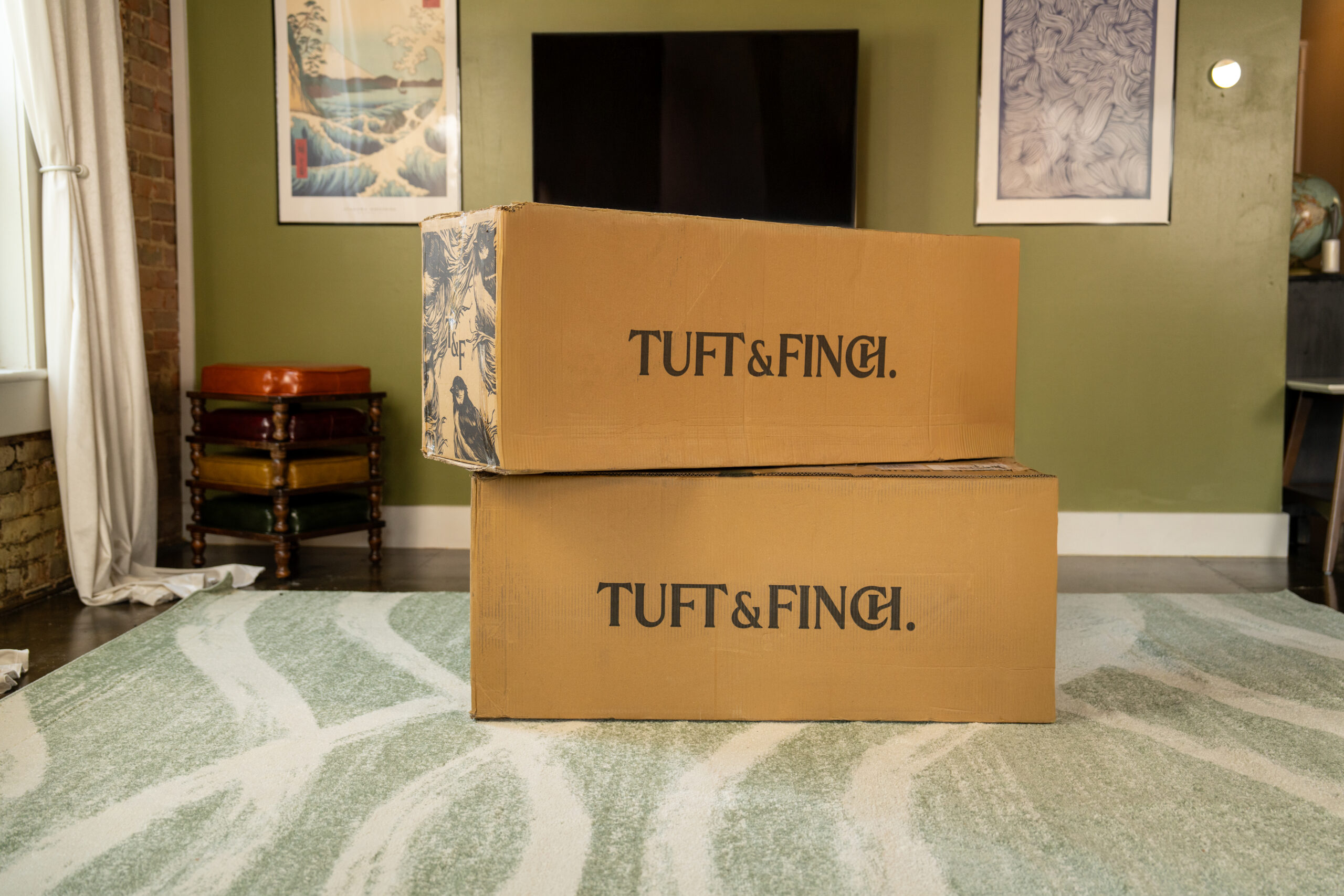 Two large boxes stacked ontop of each other in a living room that say tuft & Finch