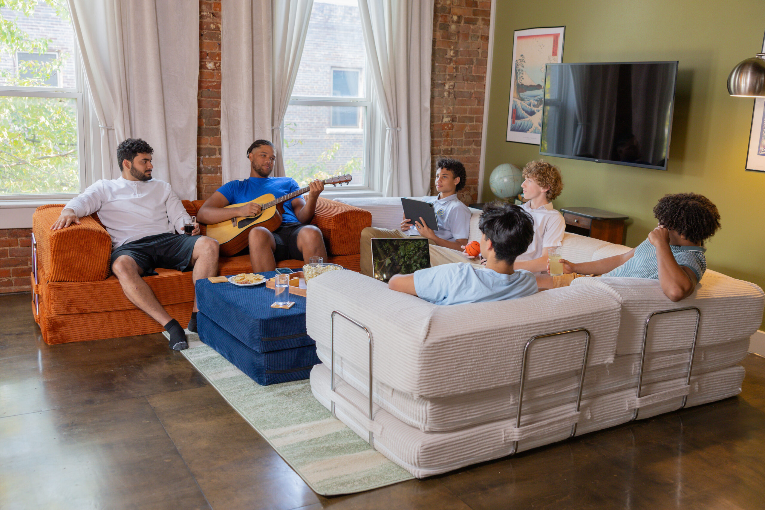 Living room with couches around an ottoman with 5 young men hanging out.